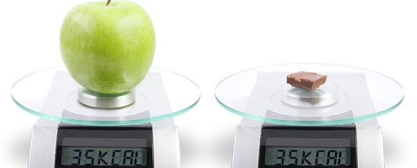 Apple on a kitchen scale, next to a square of chocolate olso on the scale. The measure is the same, and it is shown in calories. Isolated on white.