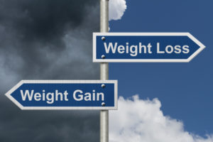 Weight Loss versus Weight Gain, Two Blue Road Sign with text Weight Loss and Weight Gain with bright and stormy sky background