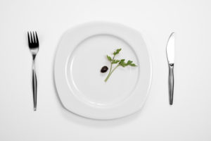 Single black olive and parsley on the middle of a plate, knife and fork.
