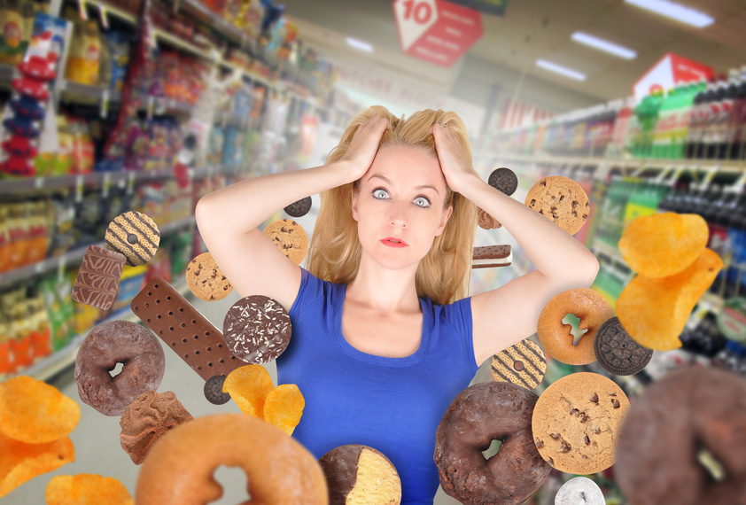 A woman has sweet food snacks around her on in a grocery store. She has fear and there are donuts and cookies. Use it for a health or diet concept.