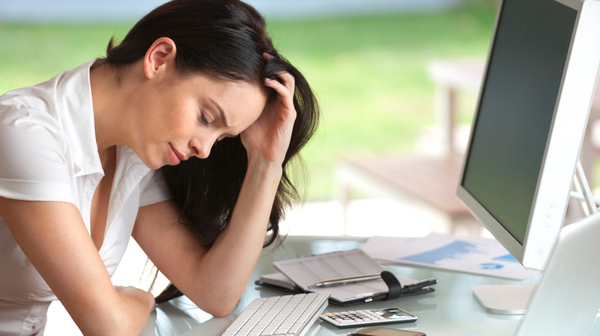 Woman looking stressed at her desk, eyes closed