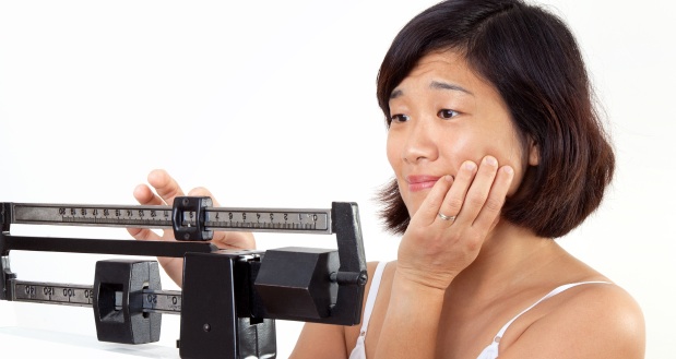 Cute middle age woman on vertical weight scale looking disappointed at her current weight