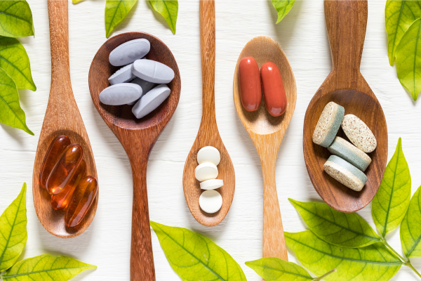 Various supplements arranged in wooden spoons with leafy accents, representing common vitamins and nutrients used in PCOS support