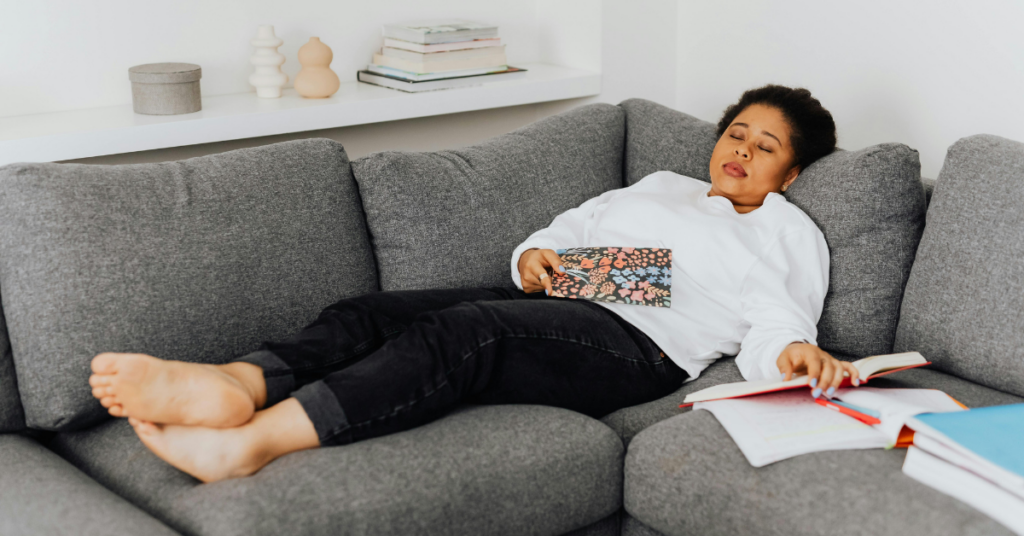 Woman lying on couch looking exhausted with open journal and books representing PCOS fatigue
