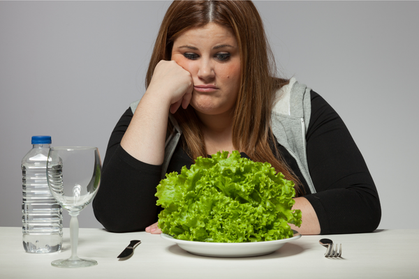 Frustrated woman staring at a plate of lettuce – symbolizing restrictive eating and diet fatigue in PCOS