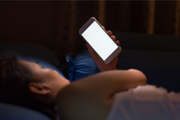 Person lying in bed at night looking at a glowing phone screen — representing poor sleep habits and blue light disruption in PCOS