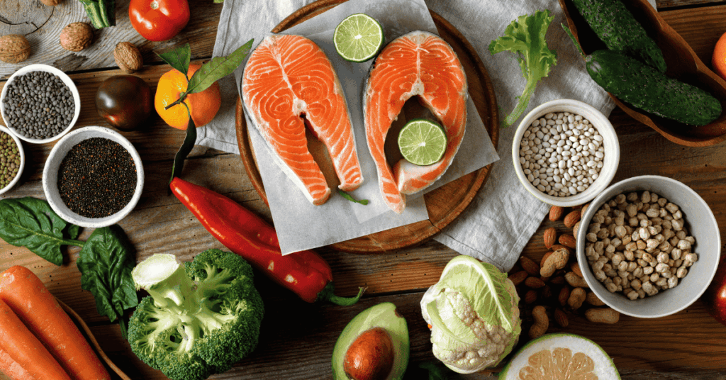 Heart-healthy foods including salmon, leafy greens, beans, nuts, avocado, and colorful vegetables arranged on a wooden table