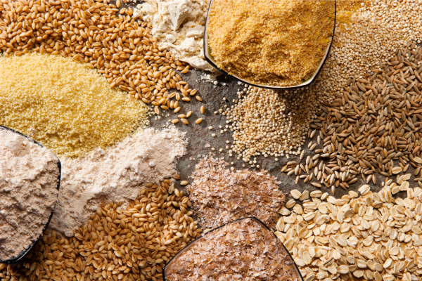 Assorted whole grains including oats, quinoa, rye, millet, wheat, bran, and flours displayed on a rustic surface.