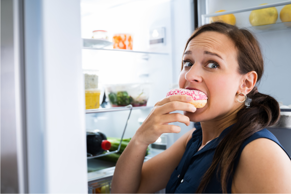 Woman stress eating a donut in front of an open fridge, highlighting gut-brain connection