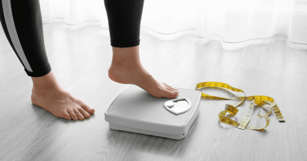 Weight loss over 40 concept — woman stepping on scale with tape measure on floor