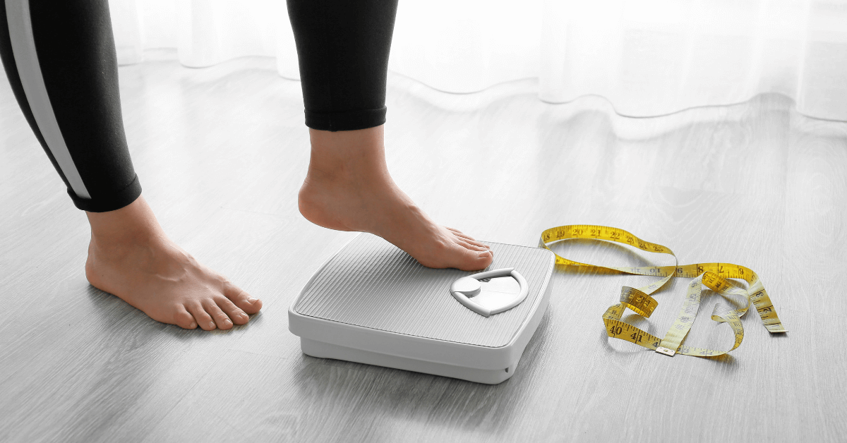 Weight loss over 40 concept — woman stepping on scale with tape measure on floor