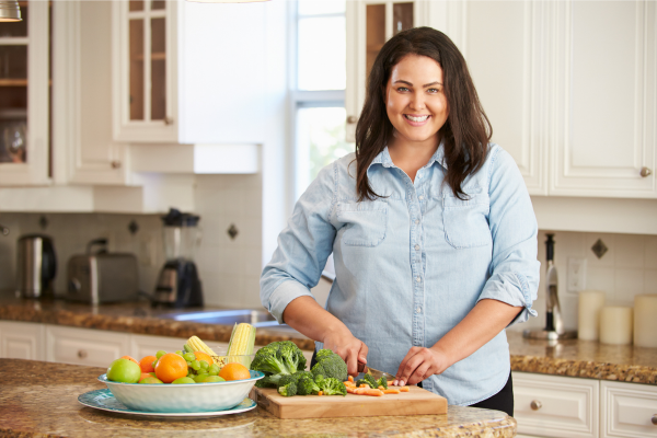 Smiling woman preparing a colorful, nutrient-rich meal in her kitchen to support natural GLP-1 hormone function and healthy weight loss