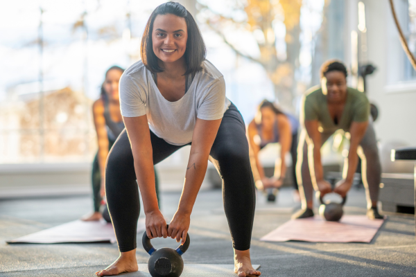 Woman lifting a kettlebell in a group fitness class to support muscle preservation and energy while on GLP-1 medication for weight loss.