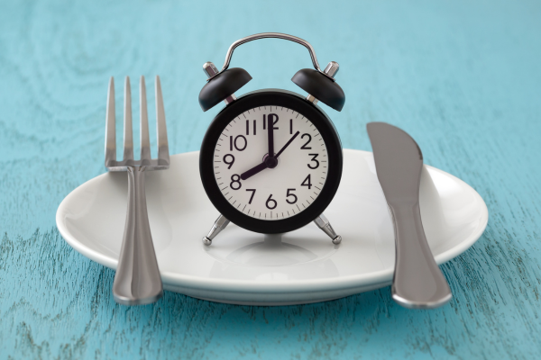 Clock on a plate with fork and knife symbolizing meal timing or intermittent fasting for weight loss
