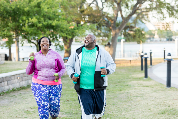 "Smiling man and woman walking outdoors with hand weights, showing movement as part of a healthy lifestyle."
