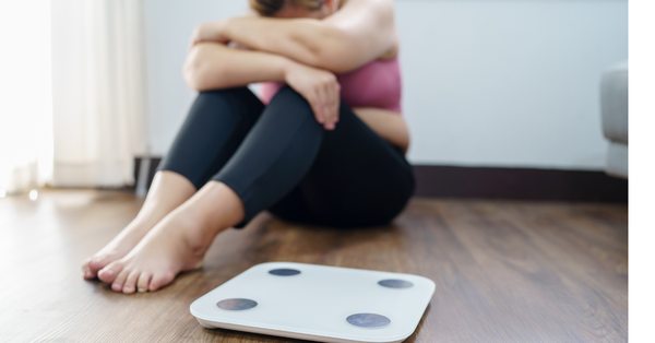 Person sitting on the floor next to a scale, representing not losing weight while using GLP-1 medication