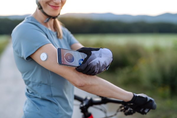 Woman wearing a continuous glucose monitor while checking blood sugar levels during outdoor cycling 