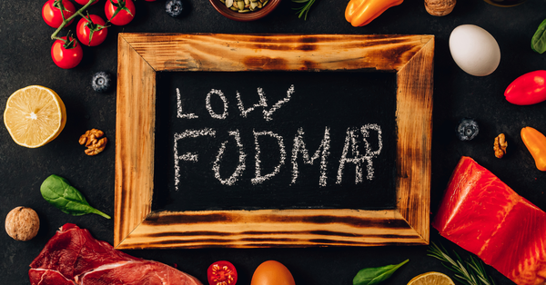 Low FODMAP diet foods for IBS shown on chalkboard surrounded by vegetables, fruit, eggs, and fish representing digestive health nutrition.