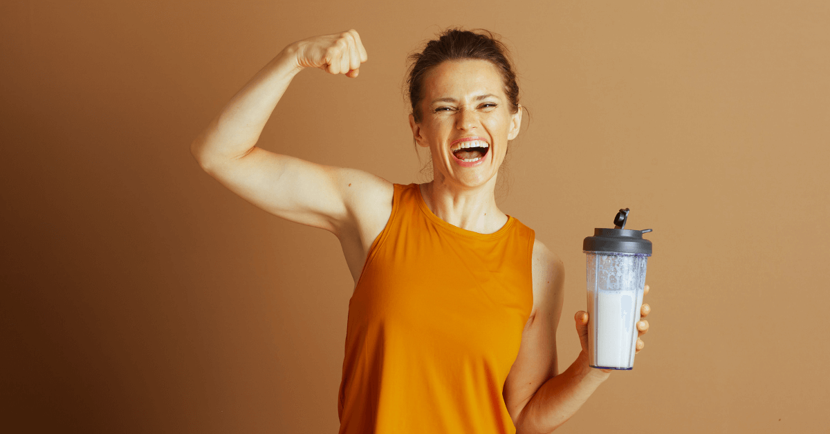 Woman flexing arm holding protein shake representing protein intake for muscle strength.