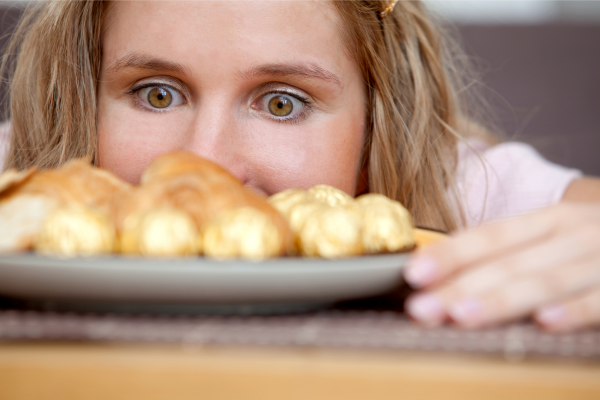 Woman looking at a plate of pastries illustrating stress-related cravings and emotional eating
